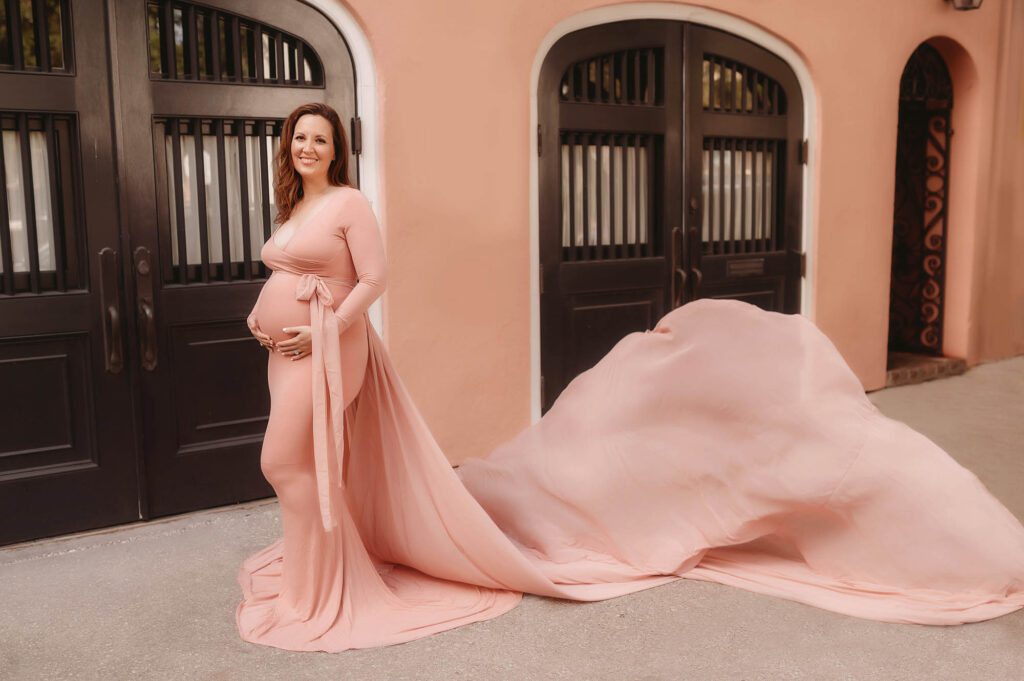 Pregnant mother embraces her baby bump during Maternity Photos on Rainbow Row in downtown Charleston, South Carolina after learning about the Best Charleston Pediatricians.