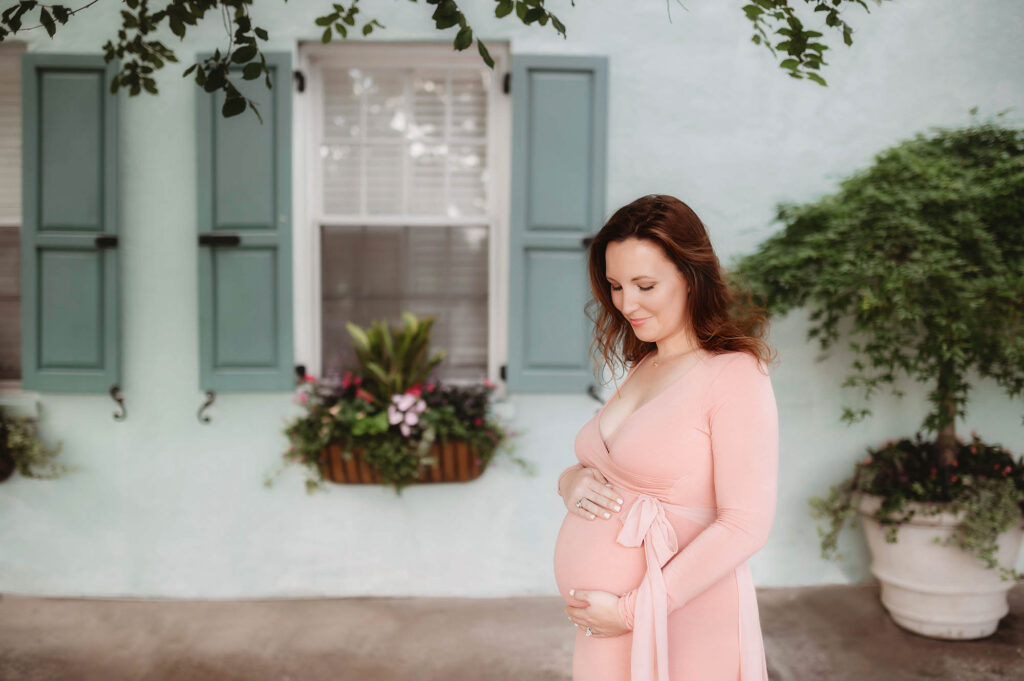 Pregnant mother embraces her baby bump during Maternity Photos on Rainbow Row in downtown Charleston, South Carolina.
