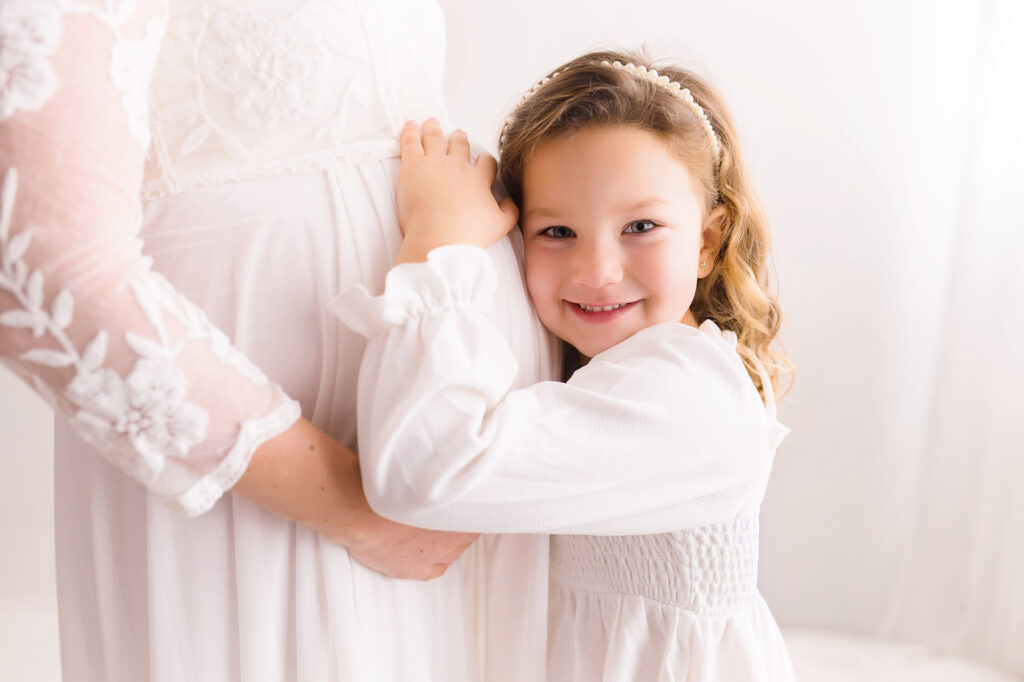 Little girl embraces her mother's pregnant belly during Studio Maternity Portraits at Holy City Babies in Charleston, SC. 
