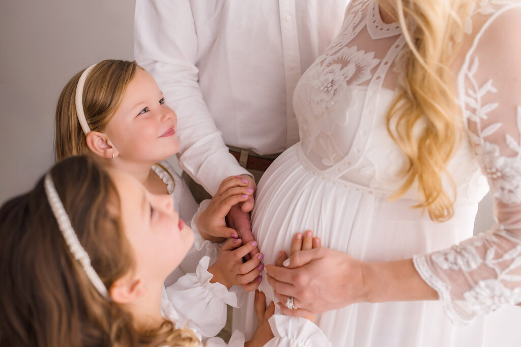 Family touches expectant mother's pregnant belly during Studio Maternity Portraits at Holy City Babies in Charleston, SC. 
