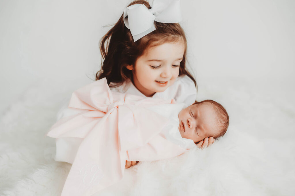 Little girl gazes at her baby sister during Studio Newborn Portrait Session at Holy City Babies Portrait Studio in Charleston, SC. 