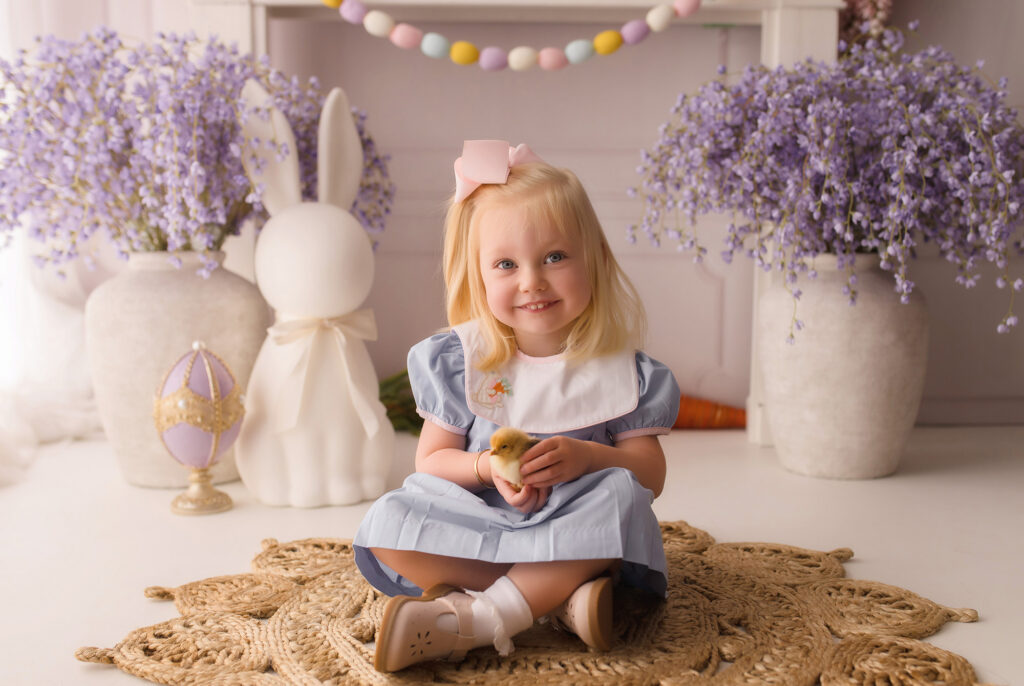 Little girl holds a baby chic during Easter Mini Session at Holy City Babies Portrait Studio in Charleston, SC. 