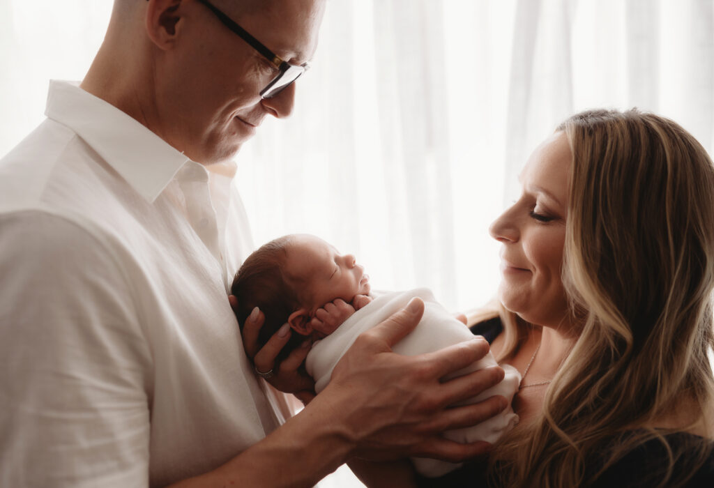After deciding betweenCharleston Studio Newborn Photography vs. In-Home Lifestyle Sessions, new parents hold their infant during a Studio Newborn Portrait Session in Charleston, SC.