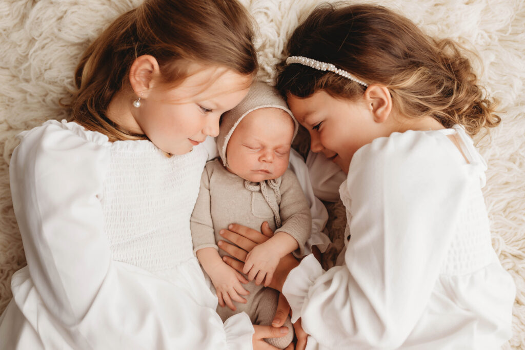 Newborn Portrait Studio in Charleston,SC studio portrait of older siblings holding sleeping newborn baby.
