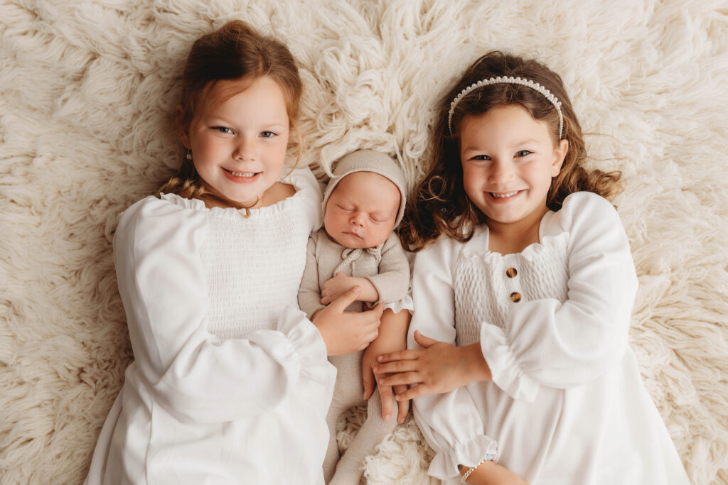 Newborn Portrait Studio in Charleston,SC studio portrait of older siblings holding sleeping newborn baby.