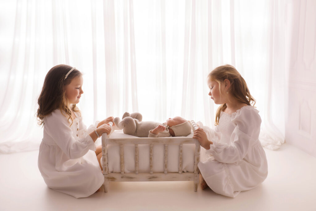 Luxury Newborn Photography Studio in Charleston,SC studio portrait of older siblings gazing at their sleeping newborn baby brother.