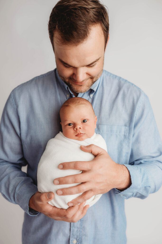 Best Newborn Photography Studio in Charleston,SC studio portrait of father holding sleeping newborn baby.