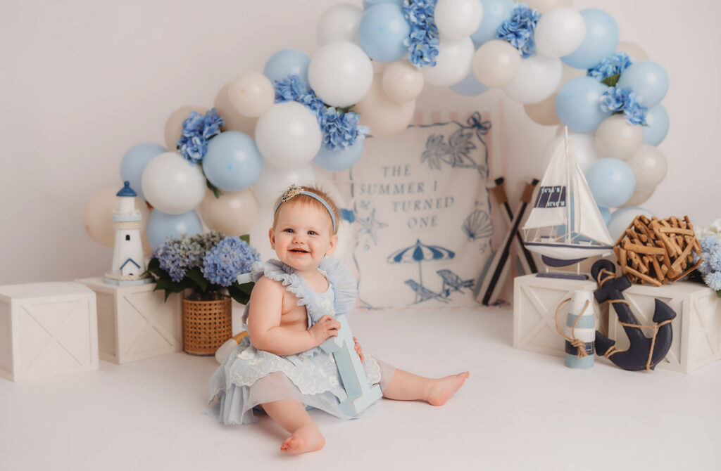 Baby smiles at the camera during their First Birthday, Milestone, Cake Smash Photoshoot at Holy City Babies Portrait Studio in Charleston, SC.