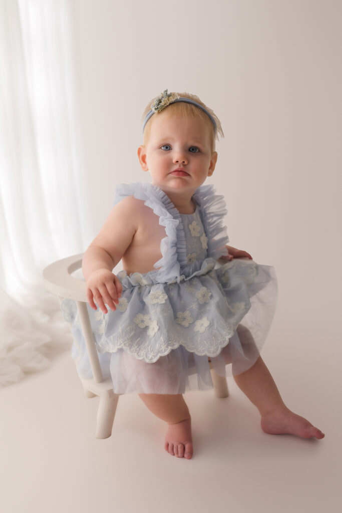 Luxury First Birthday Photography in Charleston - Baby peers at the camera during their First Birthday, Milestone, Cake Smash Photoshoot at Holy City Babies Portrait Studio in Charleston, SC.