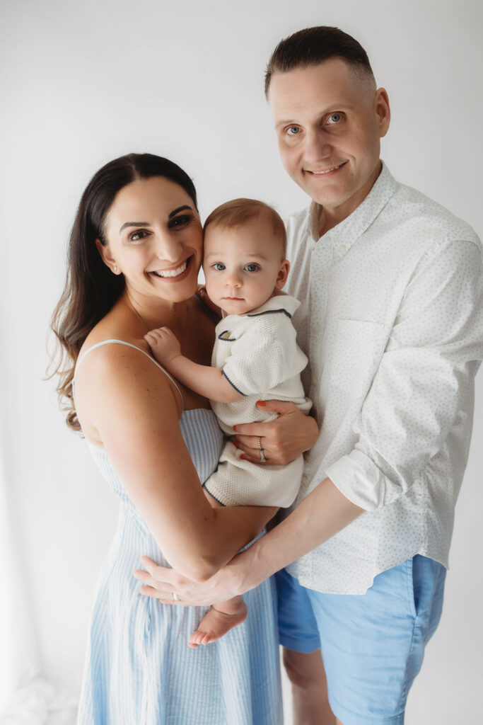 Parents embrace their baby as they celebrate first birthday with a Milestone, First Birthday Cake Smash Photoshoot at Holy City Babies Portrait Studio in Charleston, SC.