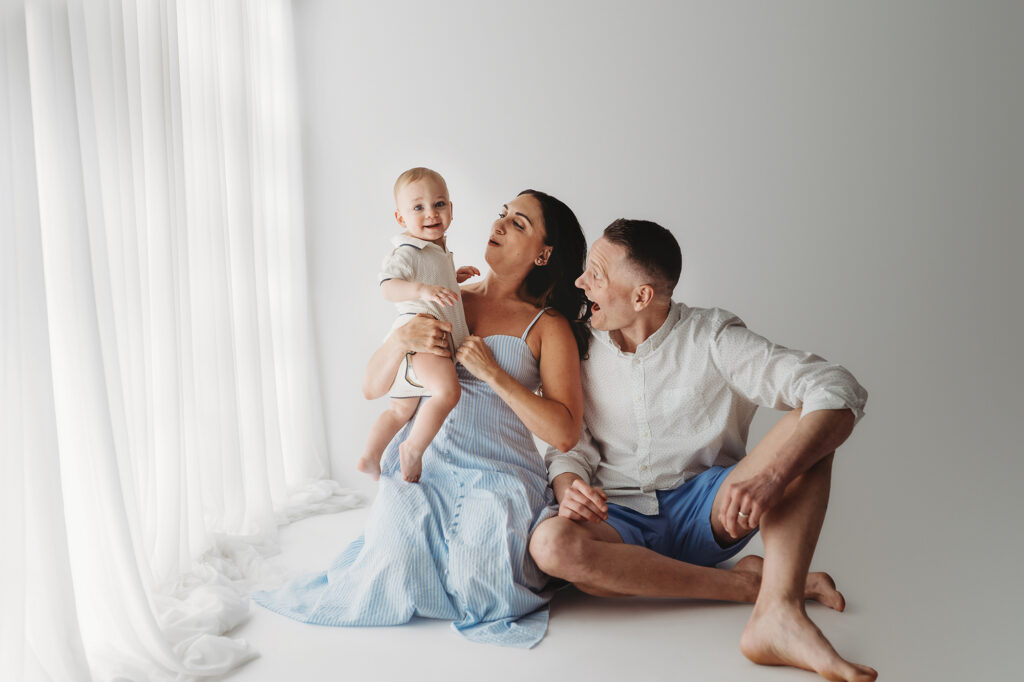 Parents embrace their baby as they celebrate first birthday with a Milestone, First Birthday Cake Smash Photoshoot at Holy City Babies Portrait Studio in Charleston, SC.