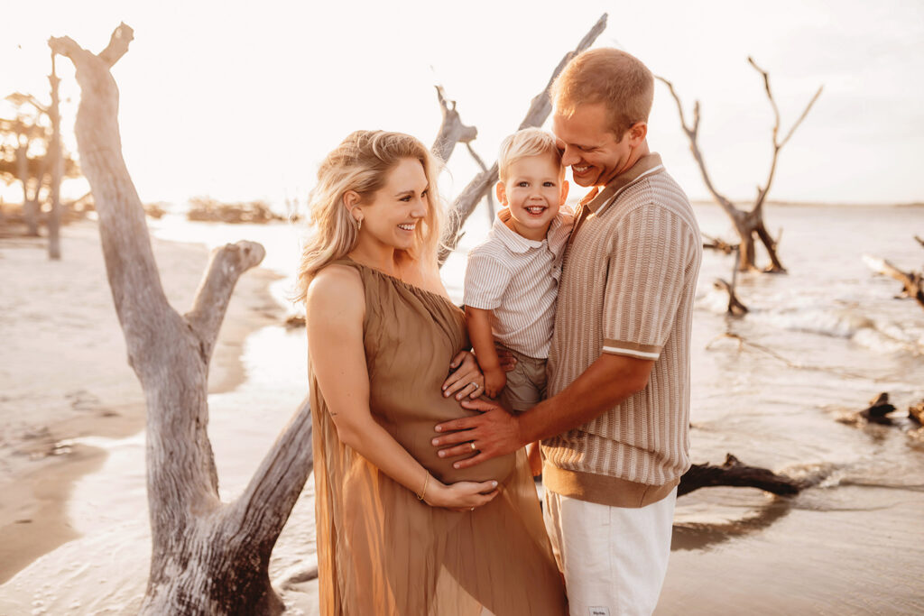 Expectant parents embrace their toddler during Maternity Portraits at Folly Beach in Charleston, SC.