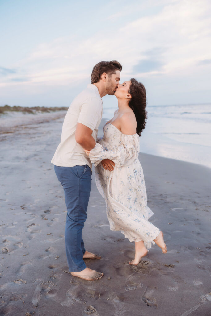 Expectant share a kiss on Folly Beach during their Maternity Portrait Session on Folly Beach after discovering The Ultimate Charleston Babymoon Planning Guide.