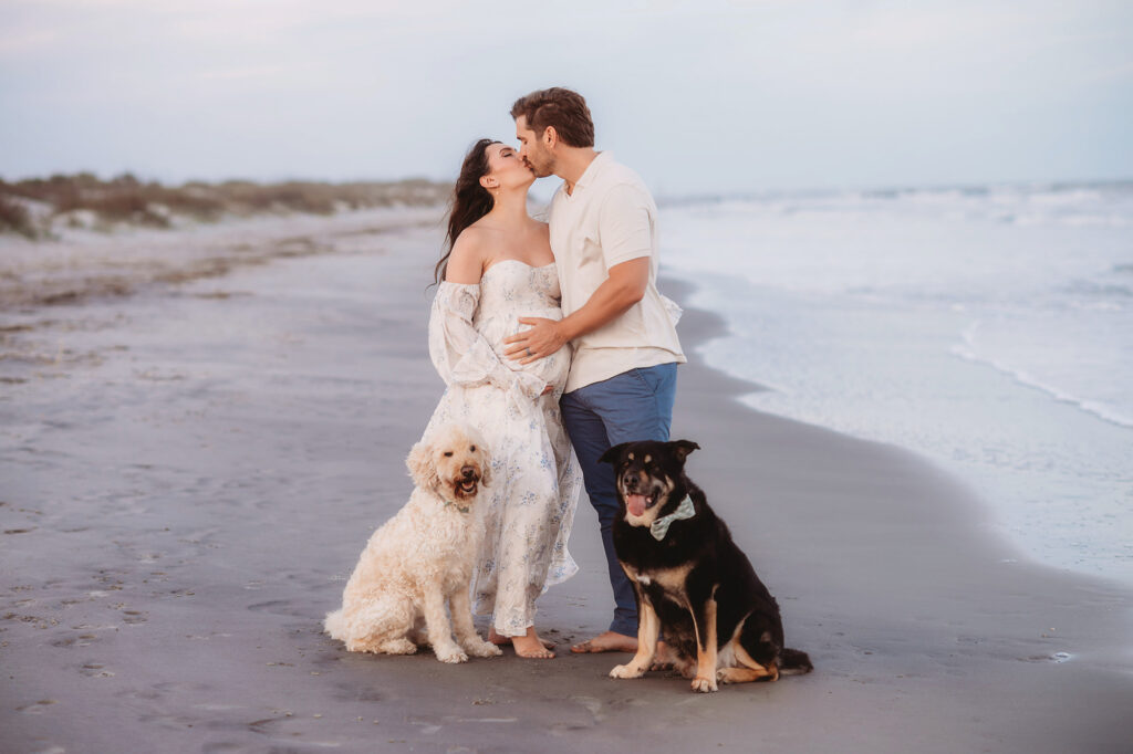 Expectant parents pose together on Folly Beach during their Maternity Portrait Session on Folly Beach after discovering The Ultimate Charleston Babymoon Planning Guide.