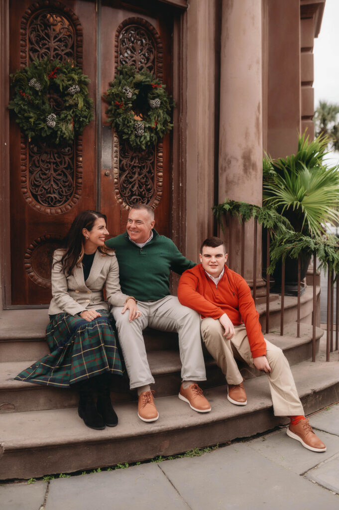 Family sits on the steps of a festively decorated restaurant during Downtown Charleston Holiday Mini Sessions.